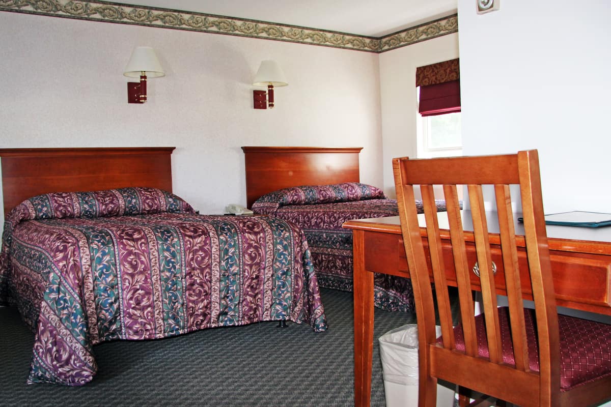 Une chambre d’hôtel avec deux lits, une chaise en bois et deux lampes fixées au mur.