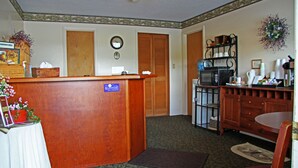 A reception area with a wooden desk, a clock on the wall, and a coffee station with a microwave and coffee maker.