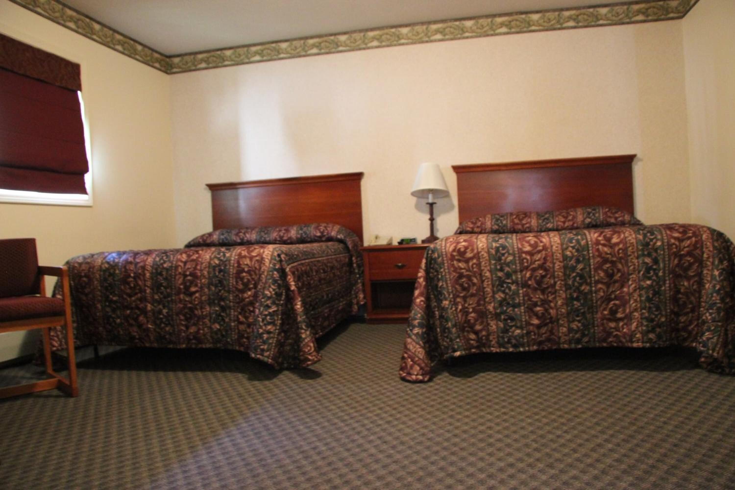 Habitación de hotel con dos camas, una mesita de noche, una lámpara y una silla.