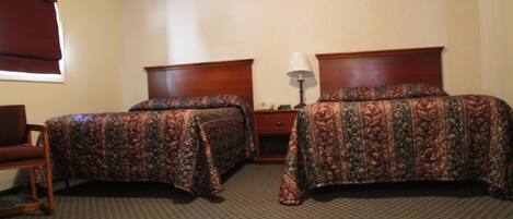 Habitación de hotel con dos camas, una mesita de noche, una lámpara y una silla.
