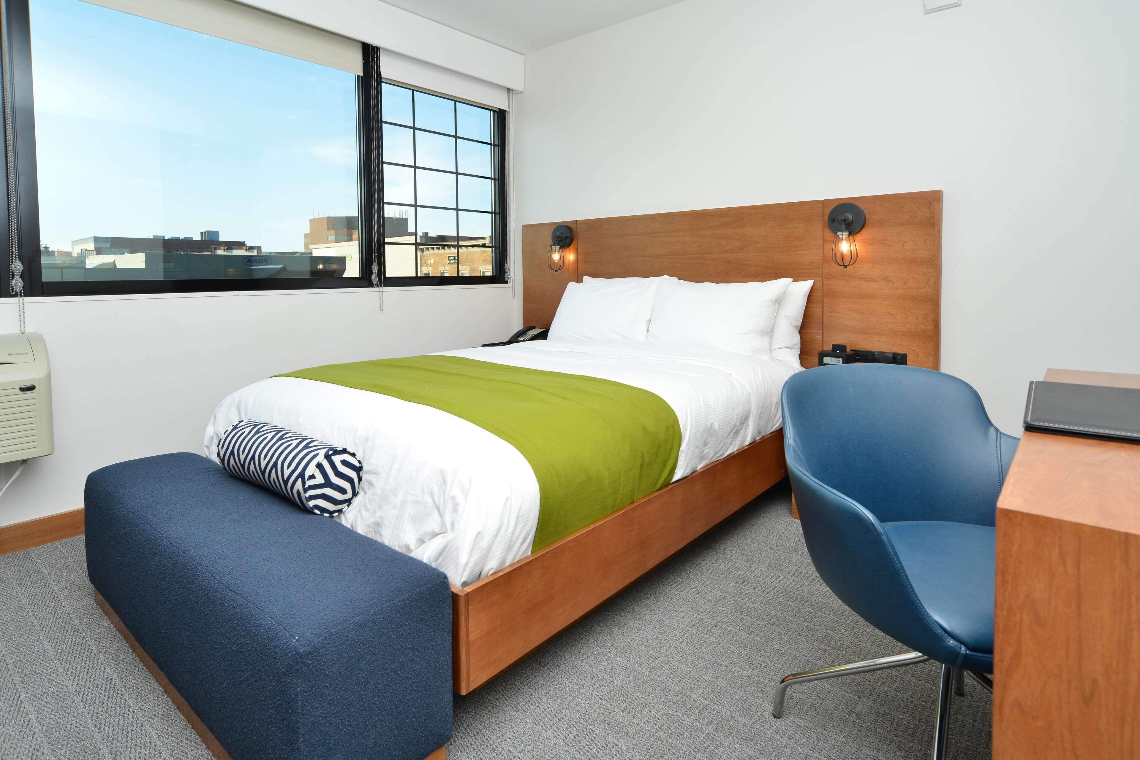 A hotel room with a bed, a desk, a chair, and a window with a city view.