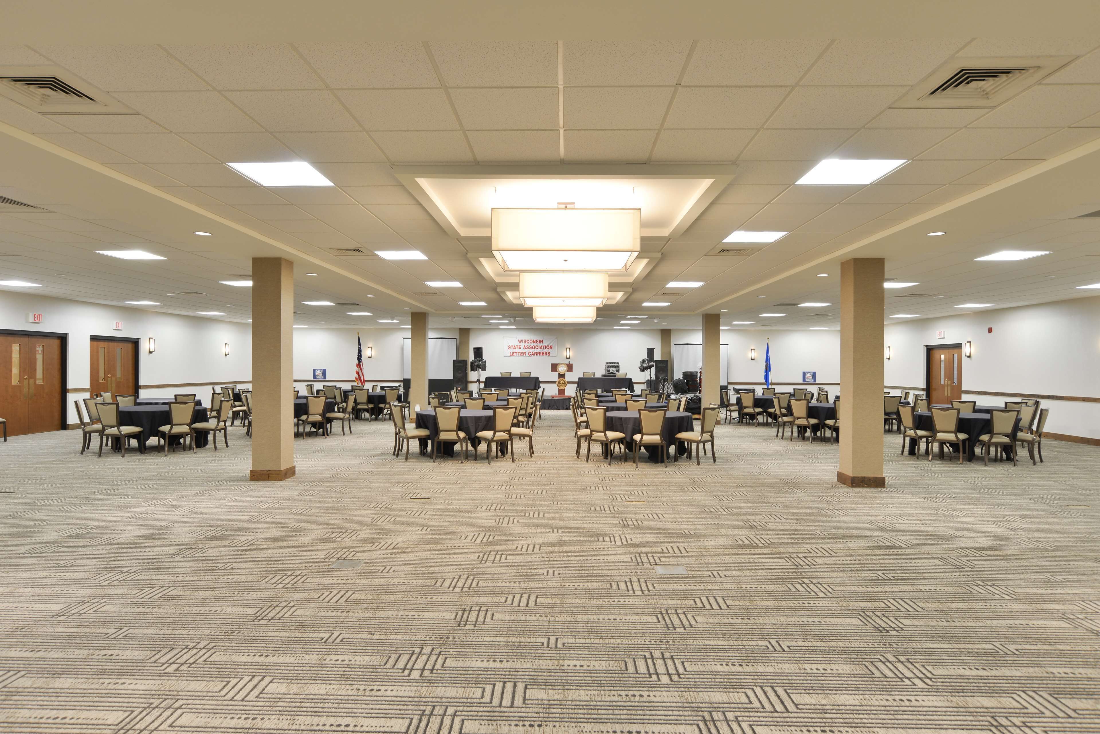 A large conference room with multiple tables and chairs, a patterned carpet, and a ceiling with recessed lighting.