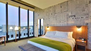 Ein Hotelzimmer mit einem großen Bett, einer Bank, einem Nachttisch und einer Wand mit Zeitungsausschnitten.