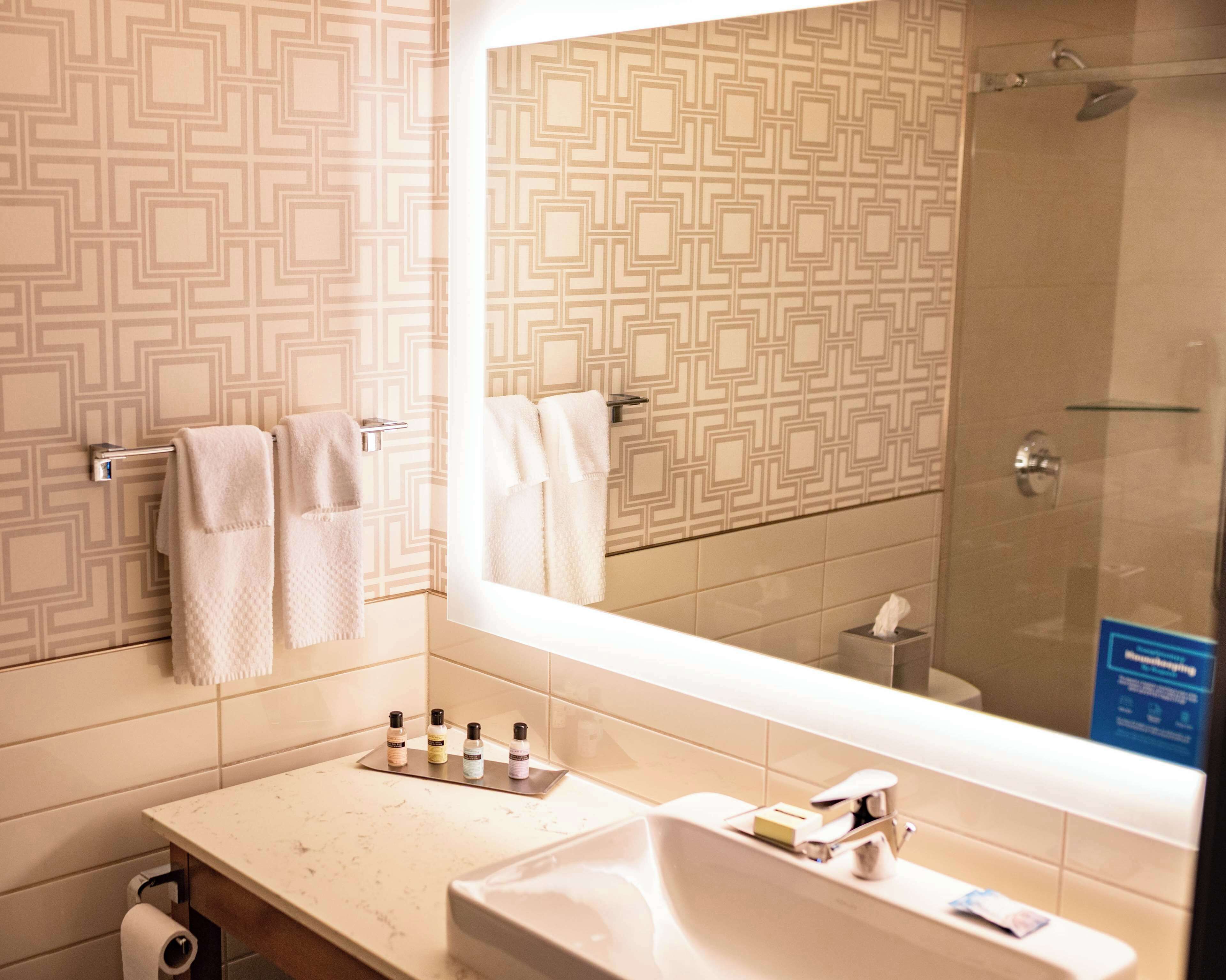 Une salle de bain avec un mur décoré de motifs, un grand miroir, un lavabo avec des articles de toilette et un espace douche.