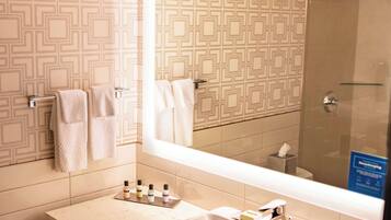 Une salle de bain avec un mur décoré de motifs, un grand miroir, un lavabo avec des articles de toilette et un espace douche.