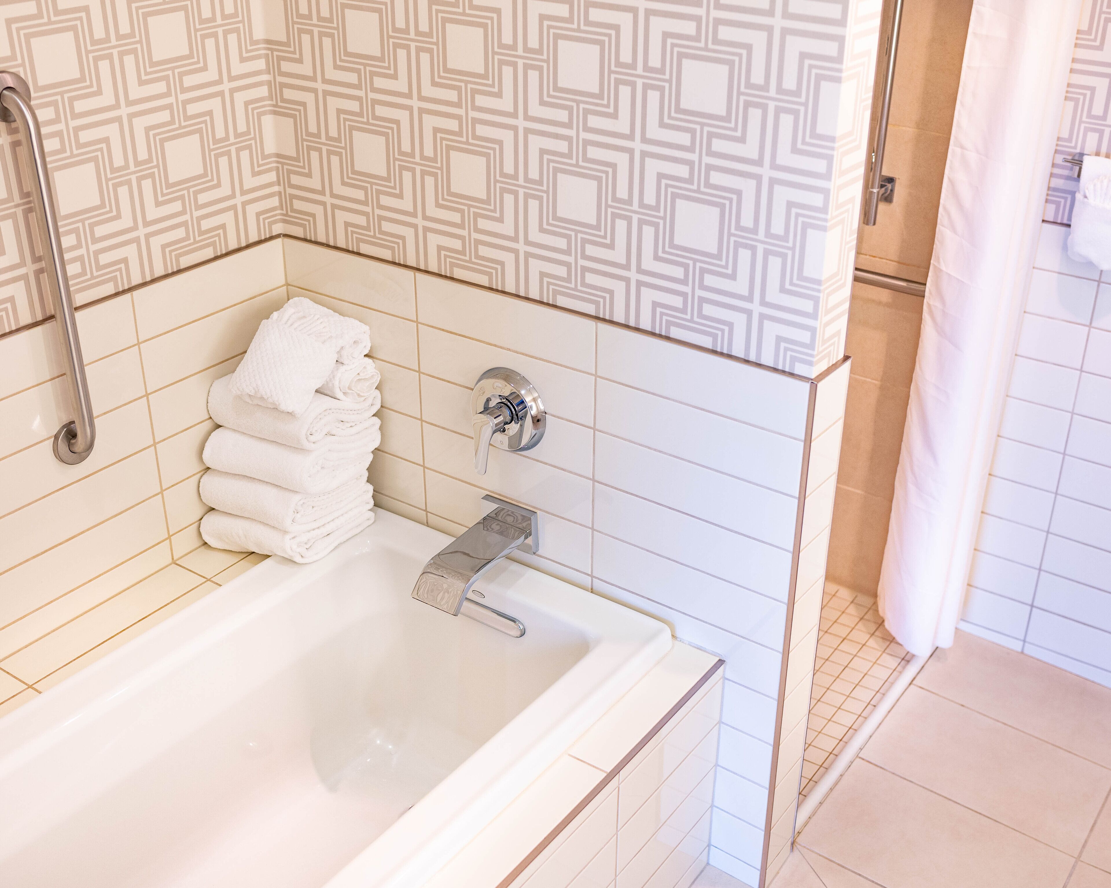 A bathroom with a bathtub, a handrail, and a stack of white towels.