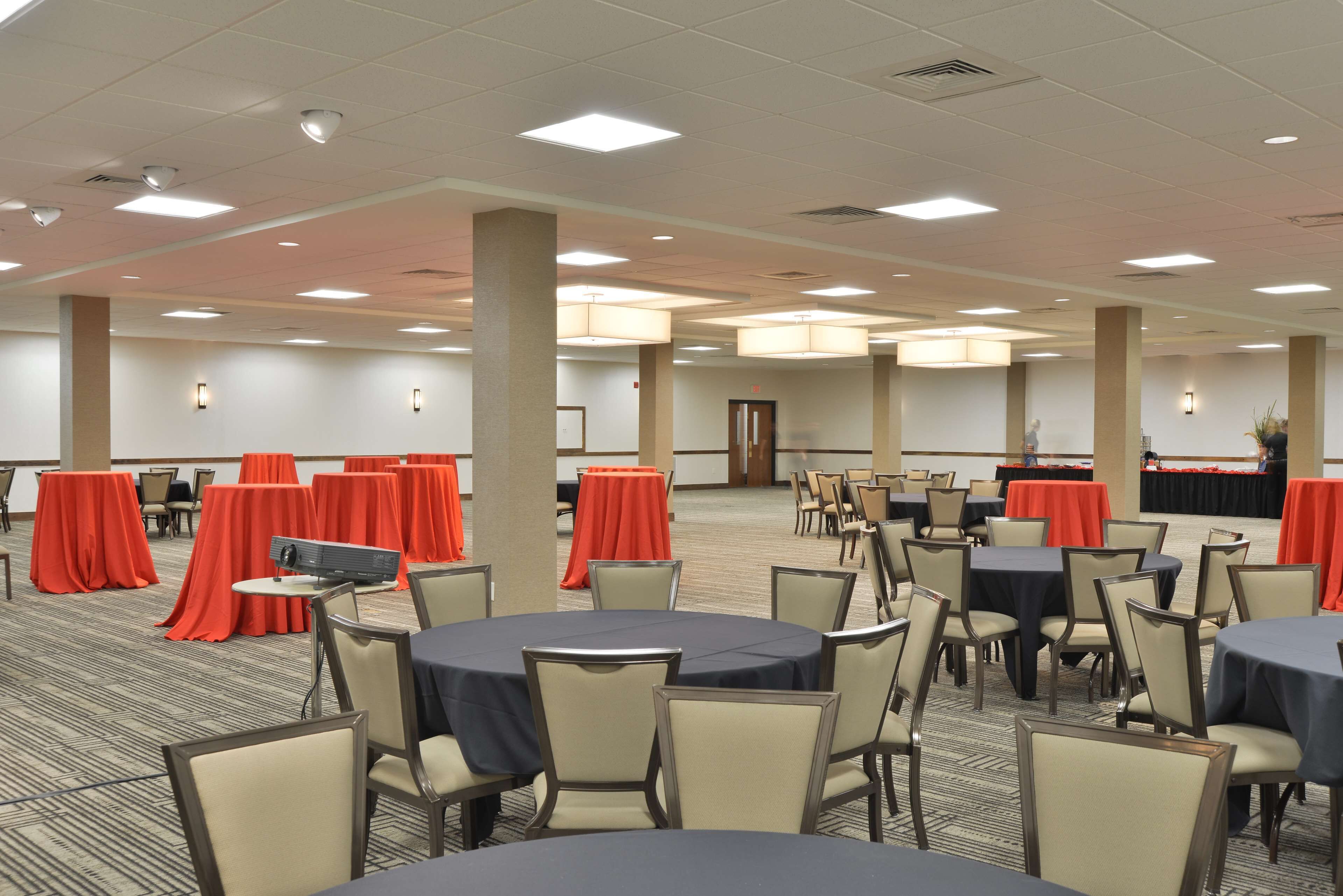 Un salón de conferencias con mesas redondas, sillas color beige y manteles rojos.