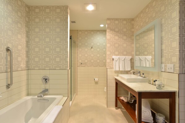 Un baño moderno con bañera, ducha y lavabo, que presenta baldosas estampadas y un tocador de madera.