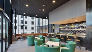 Ein modernes Café mit grünen Sitzmöglichkeiten, einer Bar und großen Fenstern, die für natürliches Licht sorgen.