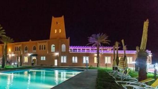A hotel with a swimming pool, palm trees, and a tower. - Hôtel Taghit Saoura (Taghit)
