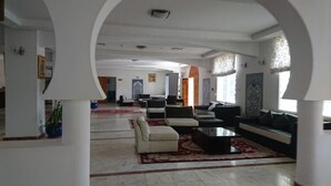 A spacious lobby with a high ceiling, a central seating area with sofas and a coffee table, and a large window providing natural light. - Hôtel Taghit Saoura (Taghit)