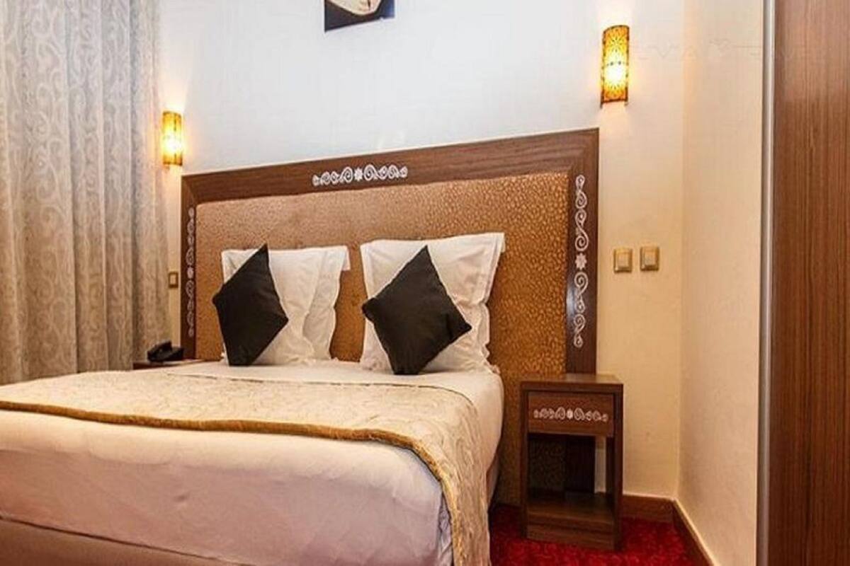 A hotel room with a large bed, two bedside lamps, a nightstand, and a wall-mounted light fixture.