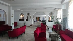 A spacious lobby with red upholstered sofas, a reception desk, and a view of the interior through arched doorways. - Hôtel Taghit Saoura (Taghit)