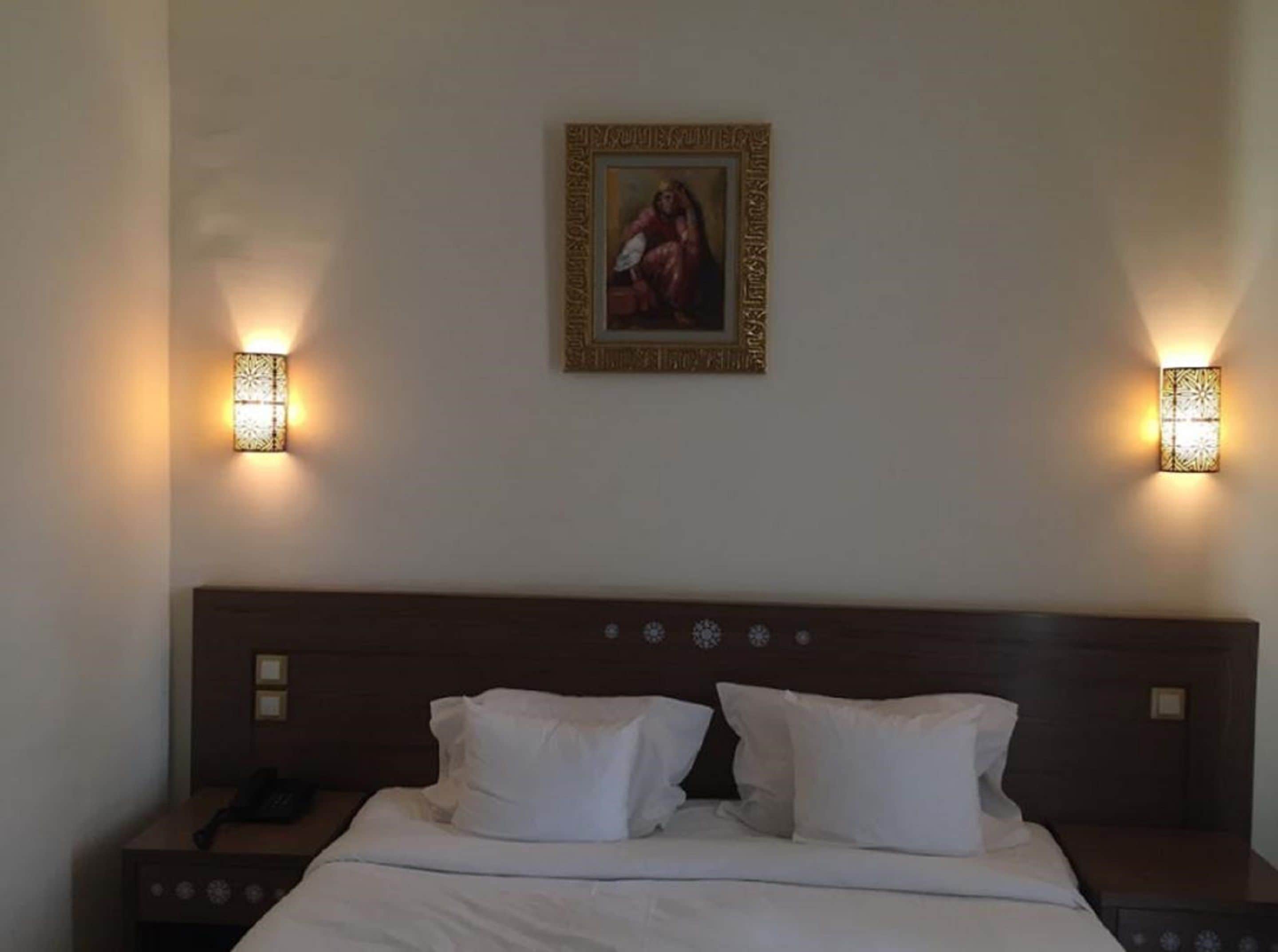 A hotel room with a bed, two bedside tables, a nightstand, and a wall-mounted painting.