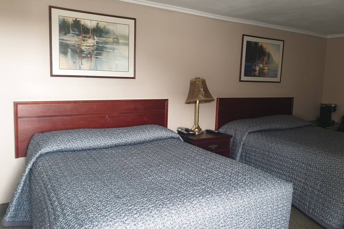 Une chambre d’hôtel avec deux lits, une table de chevet avec une lampe et deux tableaux encadrés au mur.