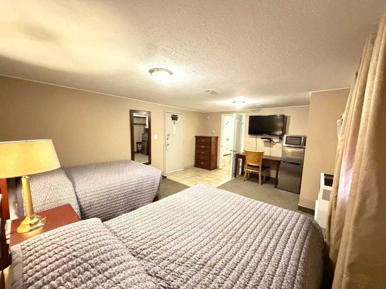 Habitación de hotel con dos camas, un escritorio, televisor y una kitchenette.