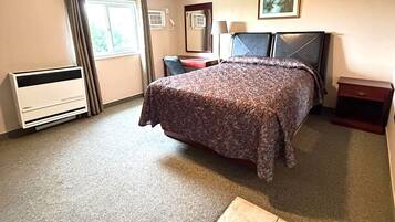 Habitación de hotel con cama, escritorio, silla, calefactor, ventana con cortinas y un cuadro en la pared.
