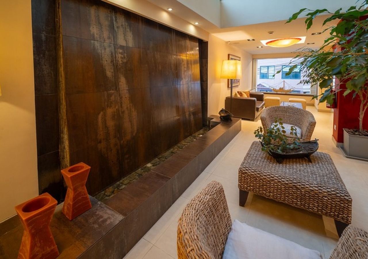 Un área de lounge moderna con una disposición de asientos, una pared con textura y una planta en maceta.