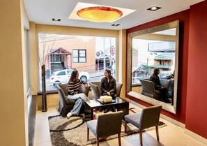 A hotel lobby with a reception desk, seating area, and large windows offering a view of the street. - Hotel Mil 810 (Ushuaia)
