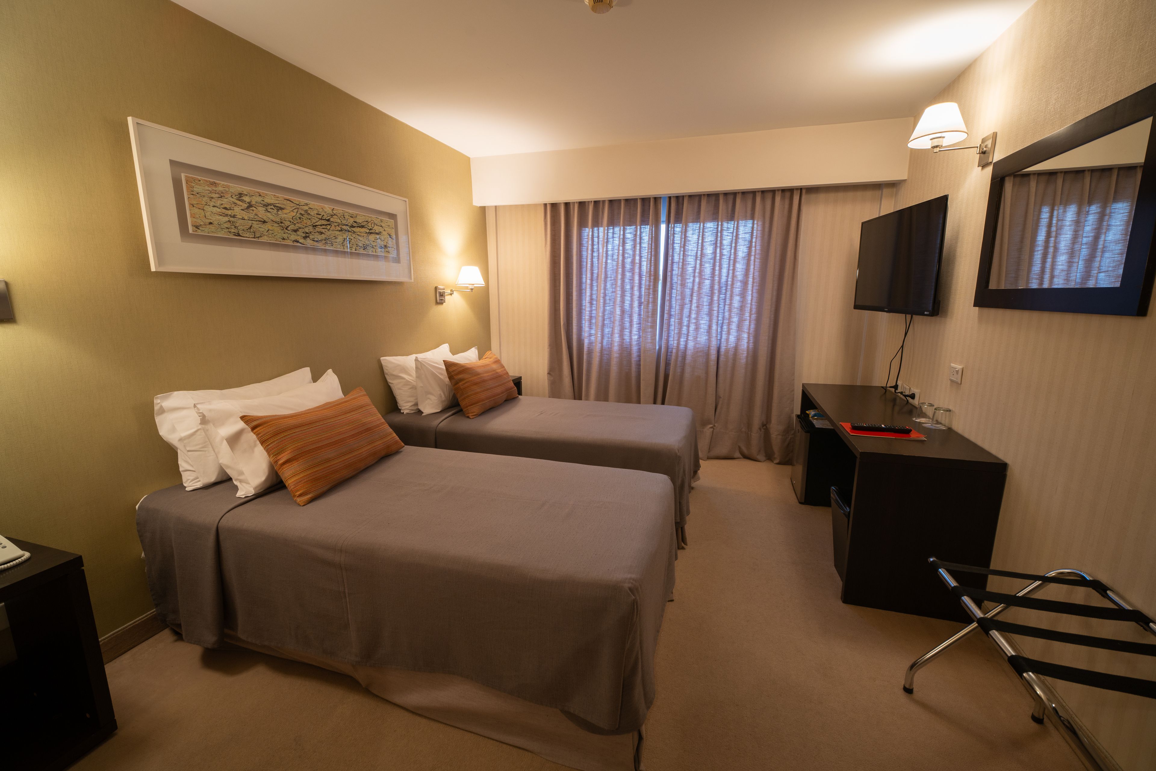 Habitación de hotel con dos camas, un escritorio, un televisor y un ventanal con cortinas.
