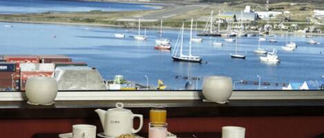 Une table à manger dressée pour le petit-déjeuner, avec vue sur un port où sont amarrés des bateaux.
