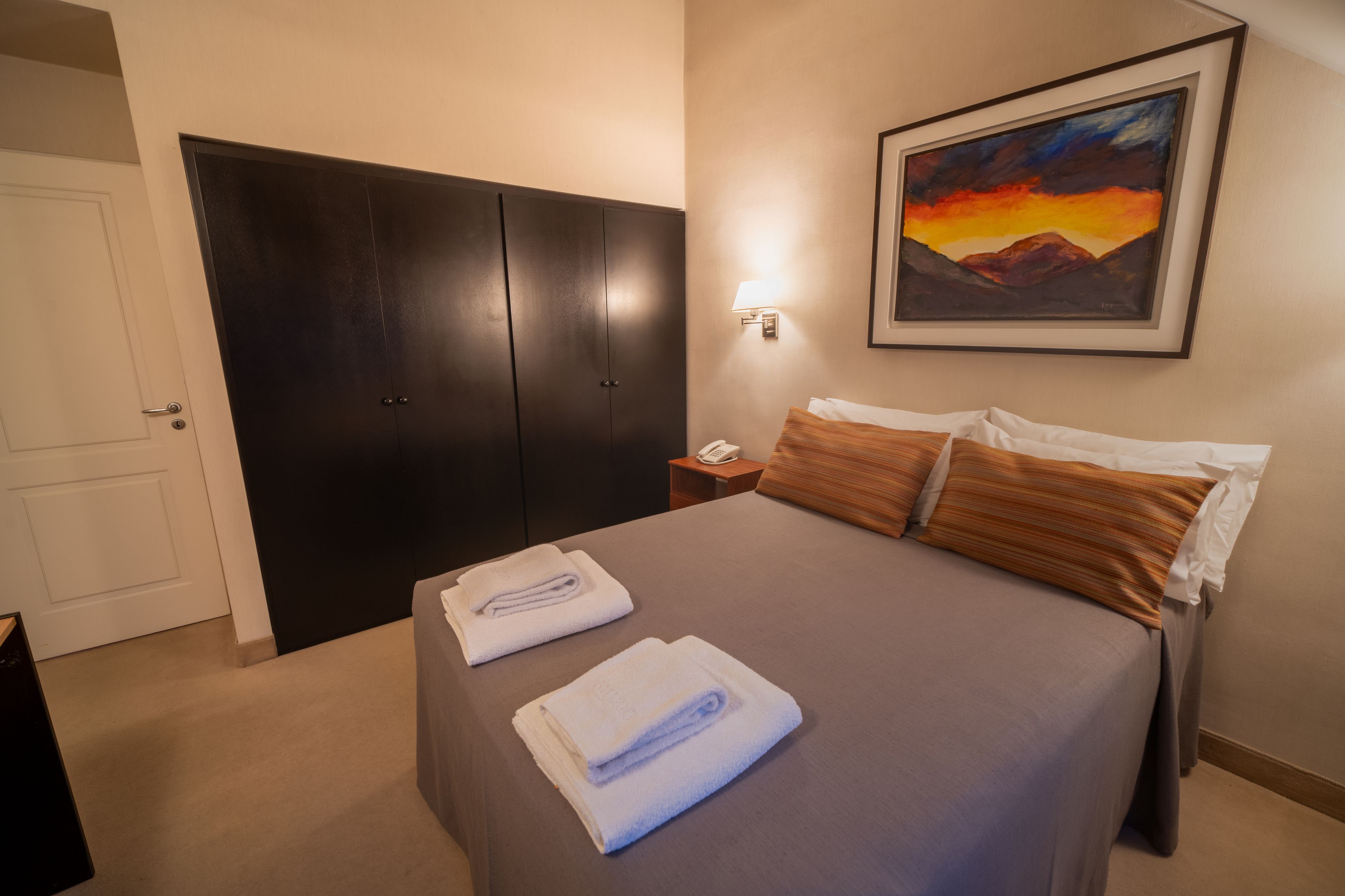 Quarto de hotel com cama, mesa de cabeceira, um quadro na parede e um guarda-roupa.