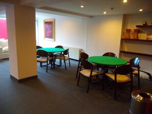 A room with two green tables and chairs, a radiator, a framed picture on the wall, and a trash can. - Hotel Mil 810 (Ushuaia)