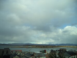 A coastal town with buildings near a body of water, mountains in the background, and a cloudy sky. - Hotel Mil 810 (Ushuaia)