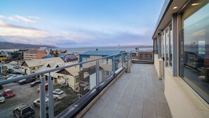 Ein Balkon mit Blick auf einen Parkplatz und Gebäude, mit Ausblick auf ein Gewässer und ferne Hügel.