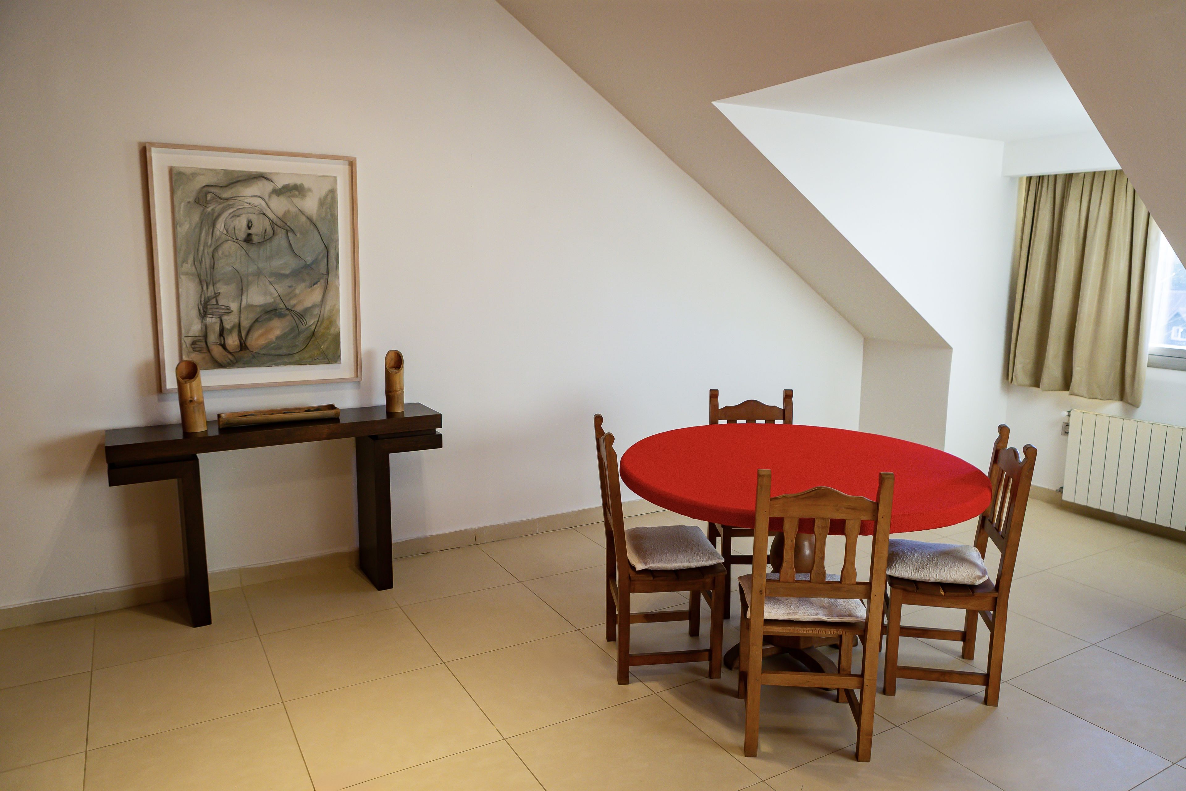 Uma área de refeições com uma mesa redonda, cadeiras, uma mesinha de madeira e um quadro na parede.