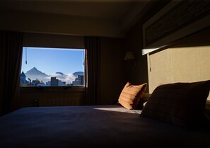 A hotel room with a bed, a window with curtains, a wall-mounted lamp, and a view of mountains. - Hotel Mil 810 (Ushuaia)