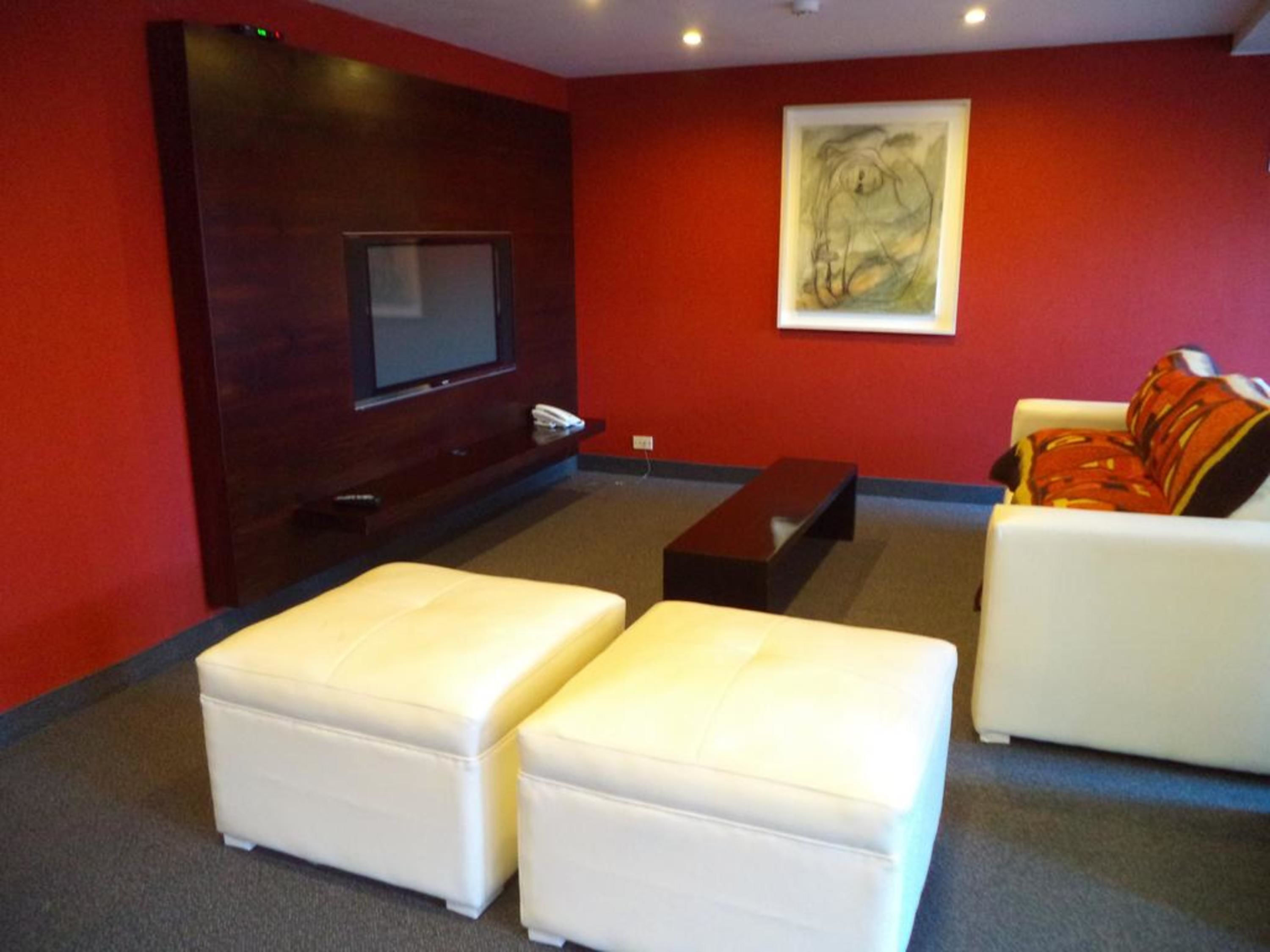 A modern living room with a flat-screen TV, a bench, and two white sofas.