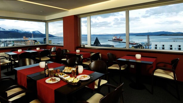 Ein Restaurant mit gedeckten Tischen, große Fenster mit Blick auf einen Hafen und Berge.
