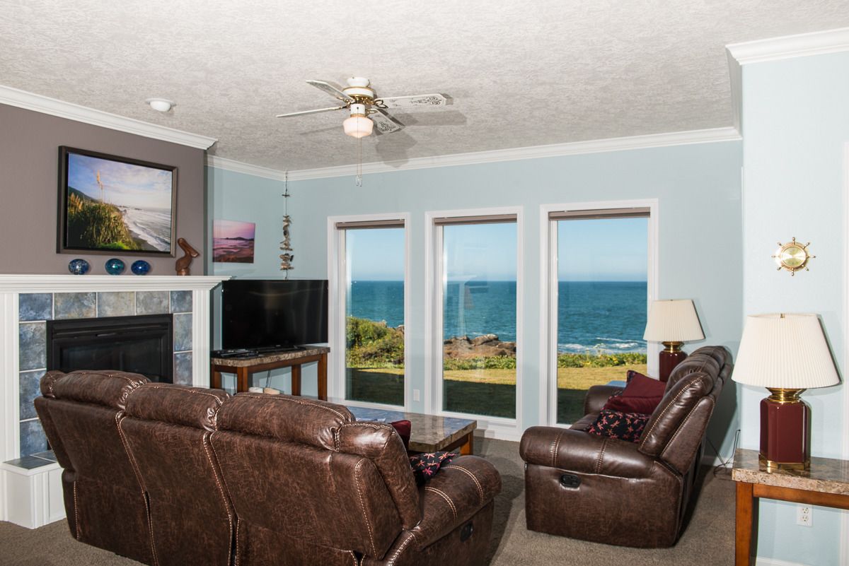 A living room with a fireplace, leather sofas, a television, and a view of the ocean.