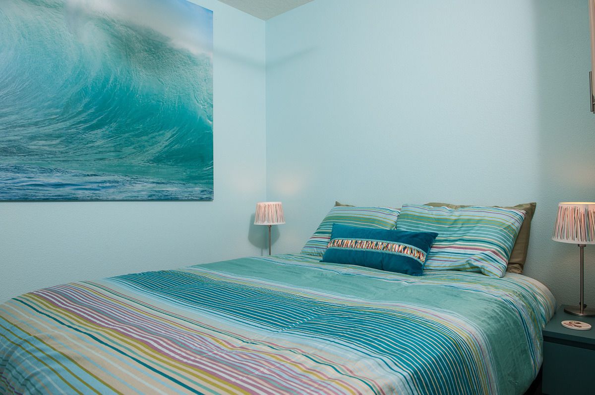 Un dormitorio con cama, almohadas y un cuadro colgado en la pared que representa una ola.