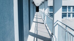 Un largo pasillo con un balcón a un lado, que conduce a un edificio de varios pisos.