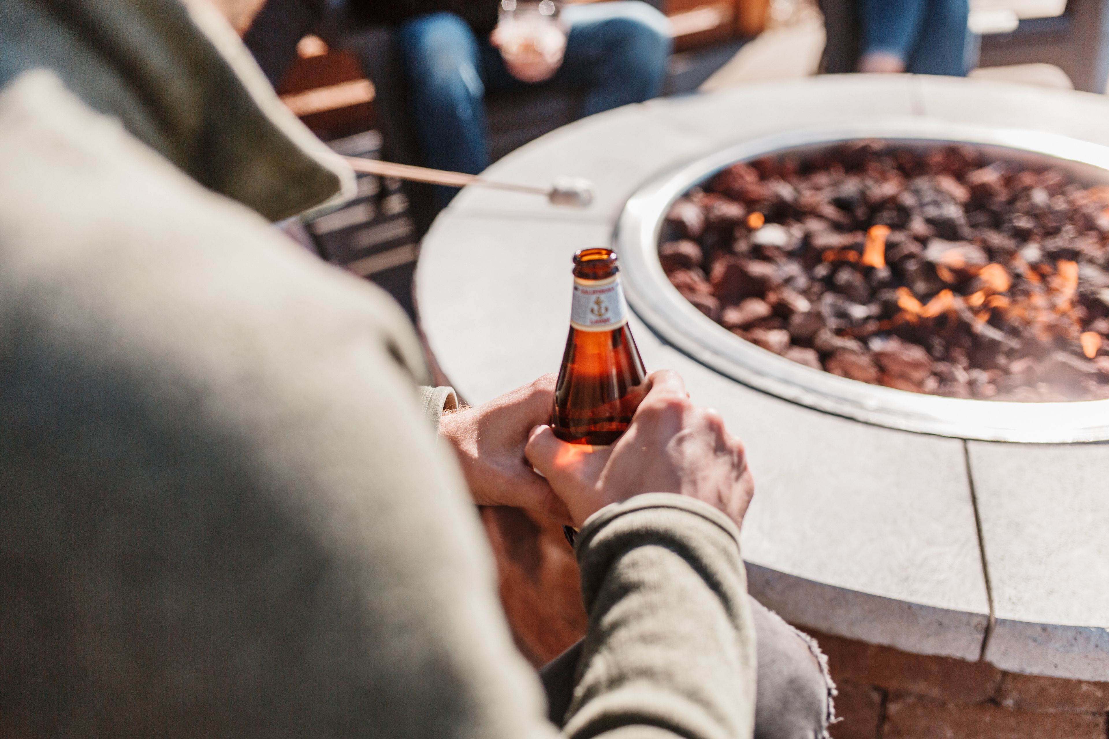 A person holding a bottle near a circular fire pit with logs.