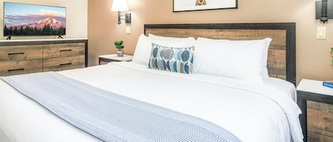 A hotel room with a large bed, a TV on a dresser, a lamp, and a framed picture of a deer on the wall.