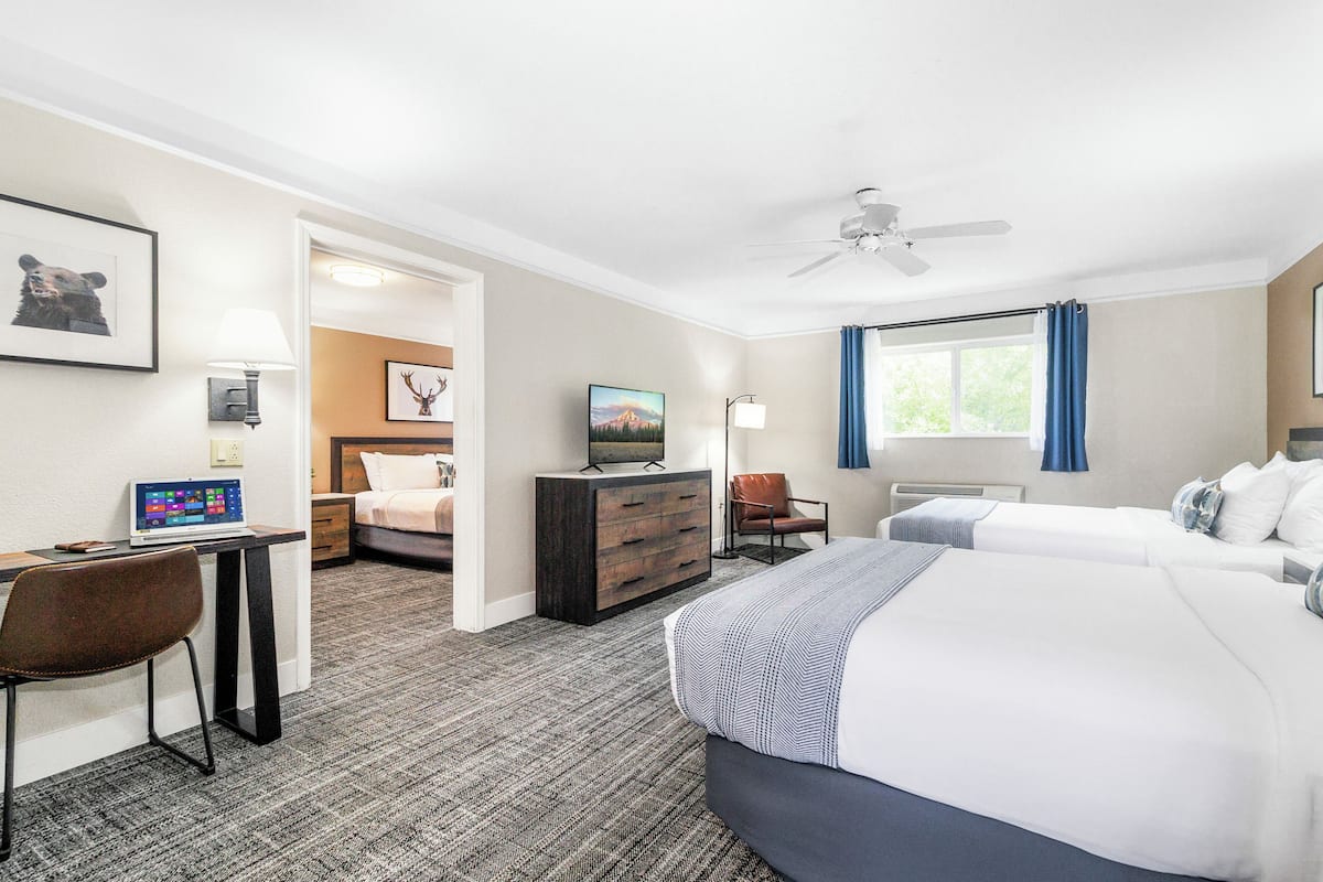 A hotel room with a desk, laptop, two beds, a dresser, and a ceiling fan.