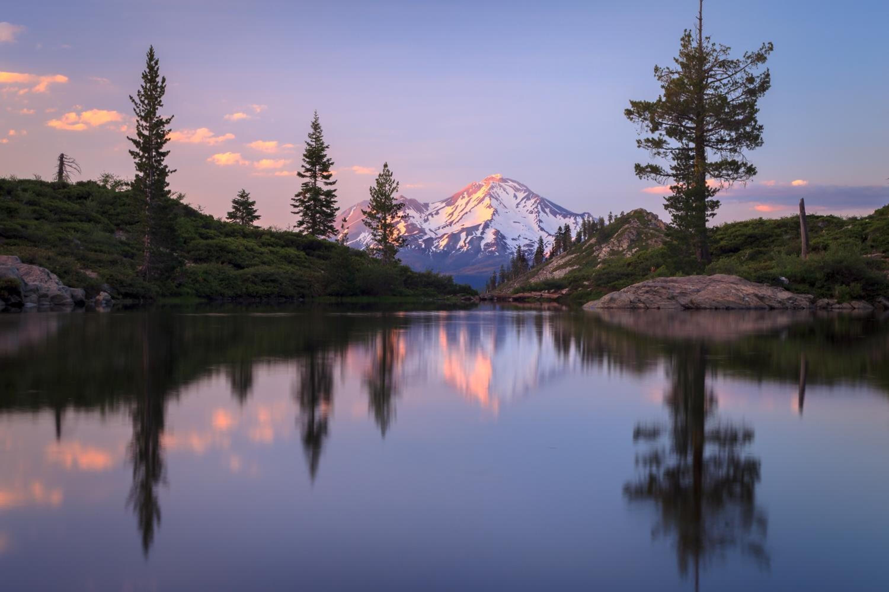 Paisaje montañoso con un lago que refleja la montaña y los árboles.