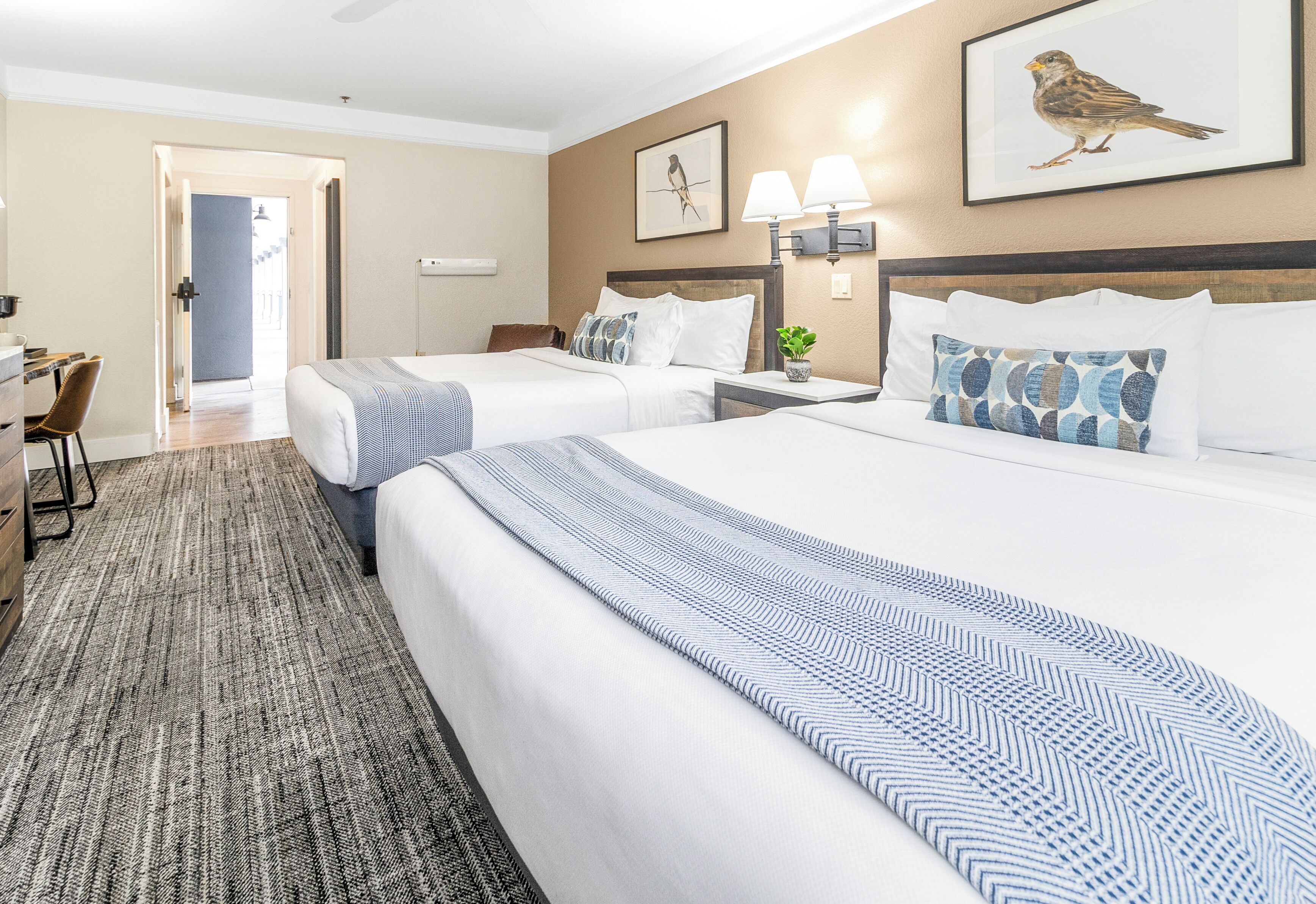 Une chambre d’hôtel avec deux lits, un bureau et une chaise. Une porte donne accès à une autre pièce.