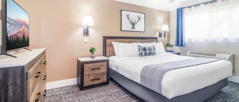 A hotel room with a bed, a TV, a ceiling fan, and a wall-mounted lamp.