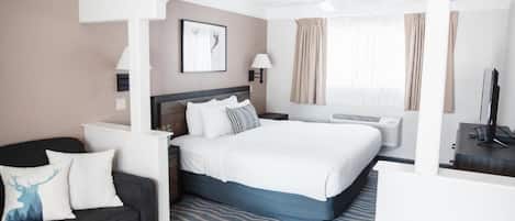 A hotel room with a bed, a sofa, a TV, a lamp, and a window with curtains.