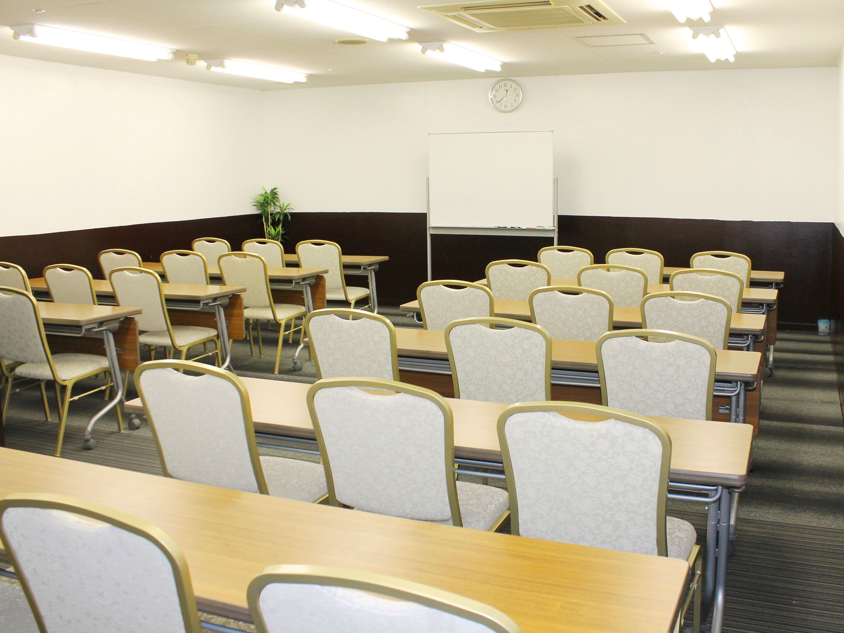 A conference room with rows of tables and chairs, a whiteboard, and a clock on the wall.