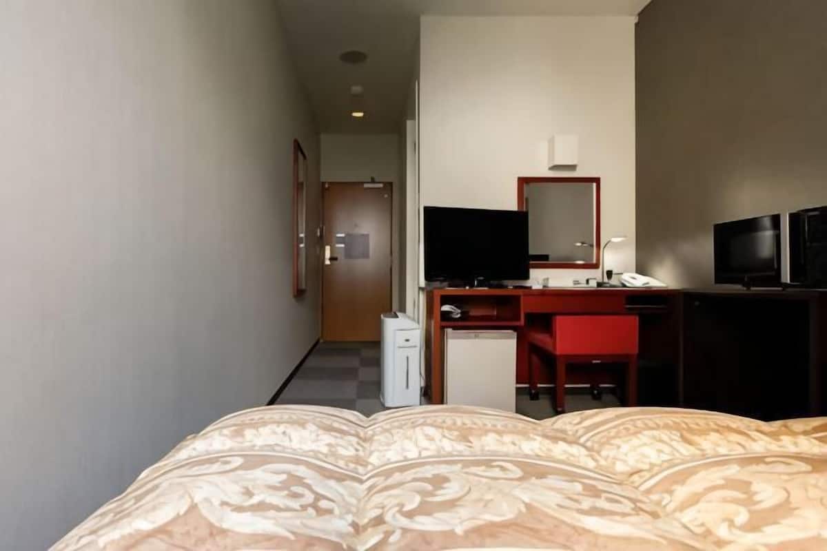 Ein Hotelzimmer mit Bett, Schreibtisch, Stuhl, Fernseher und Spiegel.