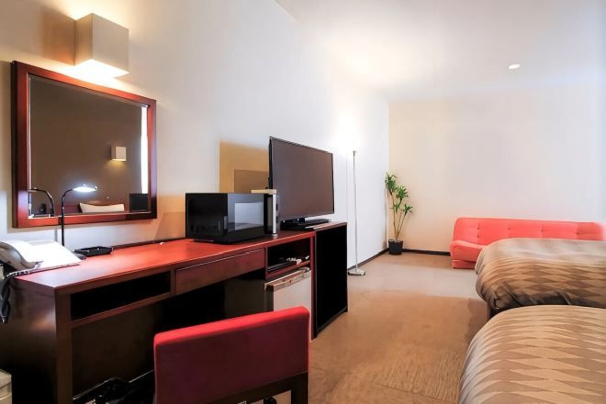 Une chambre d’hôtel équipée d’un bureau, d’une télévision, d’un lit et d’un fauteuil rouge.