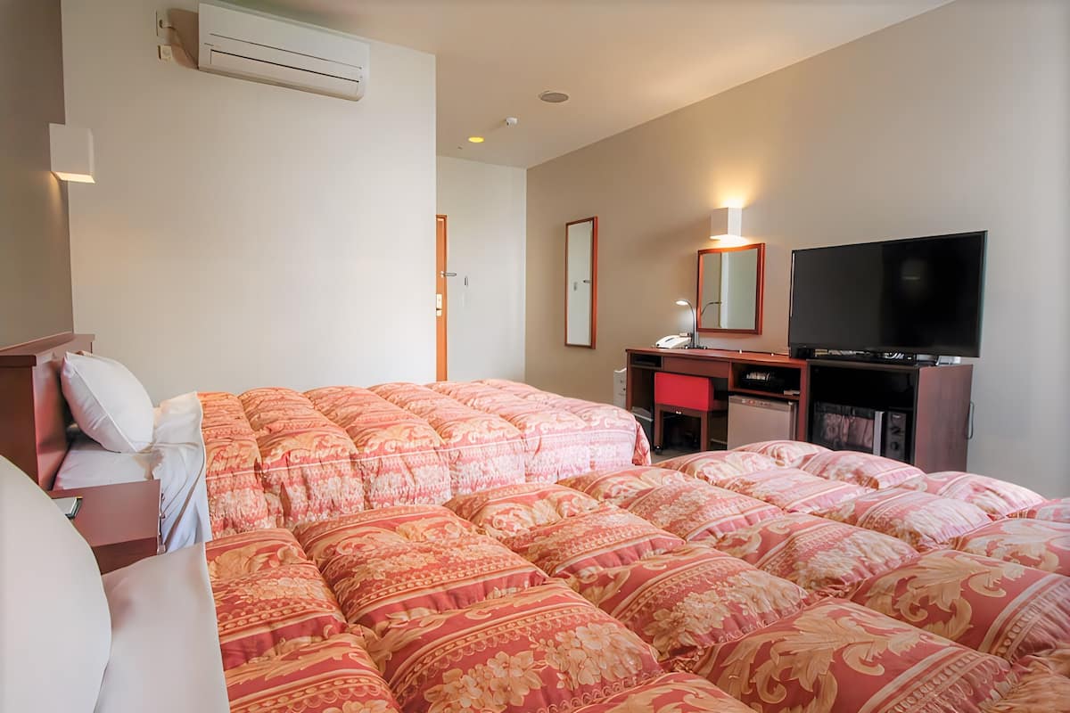 Ein Hotelzimmer mit einem großen Bett, einem Schreibtisch mit Computer, einem Flachbildfernseher und einem Kleiderschrank.