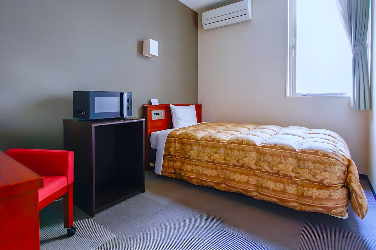 Ein Hotelzimmer mit einem Bett, einem Schreibtisch mit Computer, einem Sessel, einer Klimaanlage und einem Fenster mit Vorhängen.