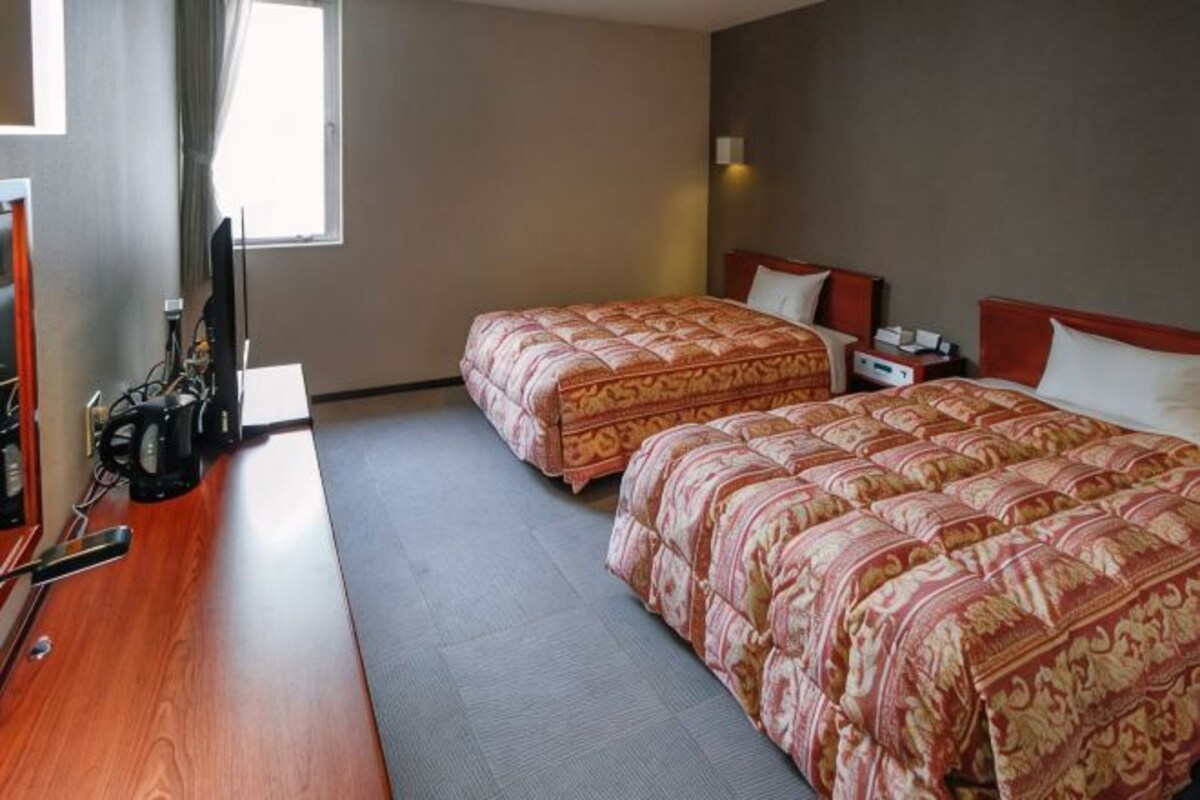 Une chambre d’hôtel avec deux lits, un bureau, une chaise, une télévision et une fenêtre.