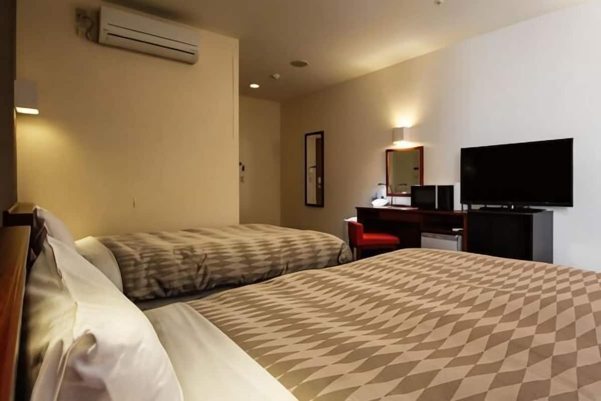 Ein Hotelzimmer mit zwei Betten, einem Schreibtisch, einem Stuhl, einem Fernseher und einer Klimaanlage.